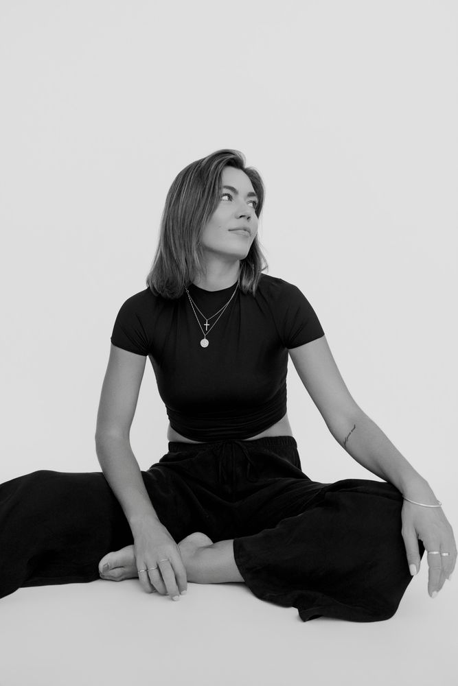 Black and white studio portrait of Danni Menzies, seated, looking to camera.