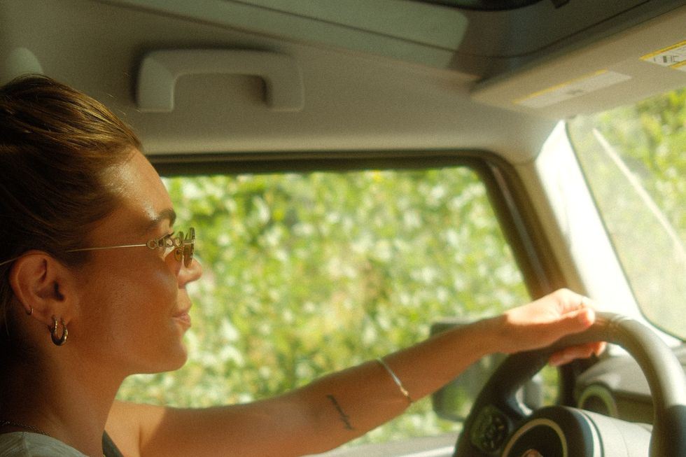 Danni Menzies at the wheel on a back road, sunglasses on.